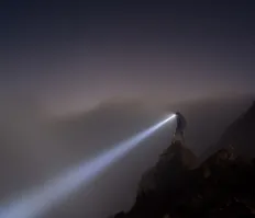 Person standing on a cliff with a flashlight