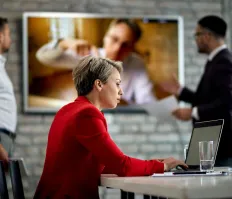 Woman working on laptop with video call in the background