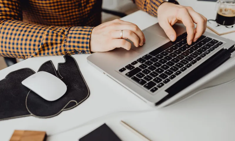 Person working on a laptop at a desk with a mouse and cup of coffee.