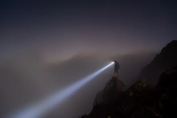 Person standing on a cliff with a flashlight