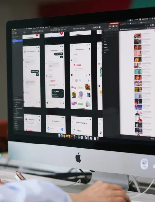 Person working at a desktop computer displaying mobile app interface designs.