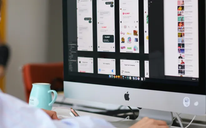 Person working at a desktop computer displaying mobile app interface designs.