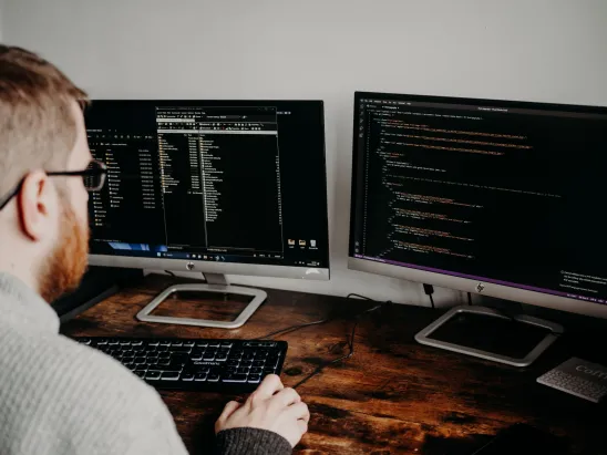Person working at a desk with two computer monitors displaying code and development files.