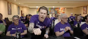 Man enthusiastically cheering, seated among others in a conference room.