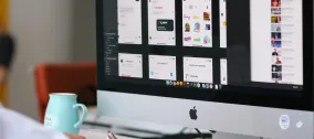 Person working at a desktop computer displaying mobile app interface designs.