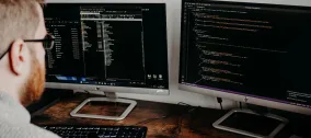 Person working at a desk with two computer monitors displaying code and development files.