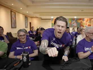 Man enthusiastically cheering, seated among others in a conference room.