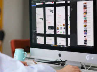 Person working at a desktop computer displaying mobile app interface designs.