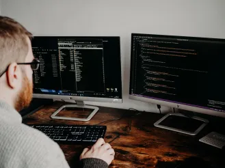 Person working at a desk with two computer monitors displaying code and development files.