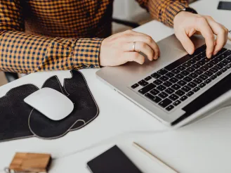 Person working on a laptop at a desk with a mouse and cup of coffee.