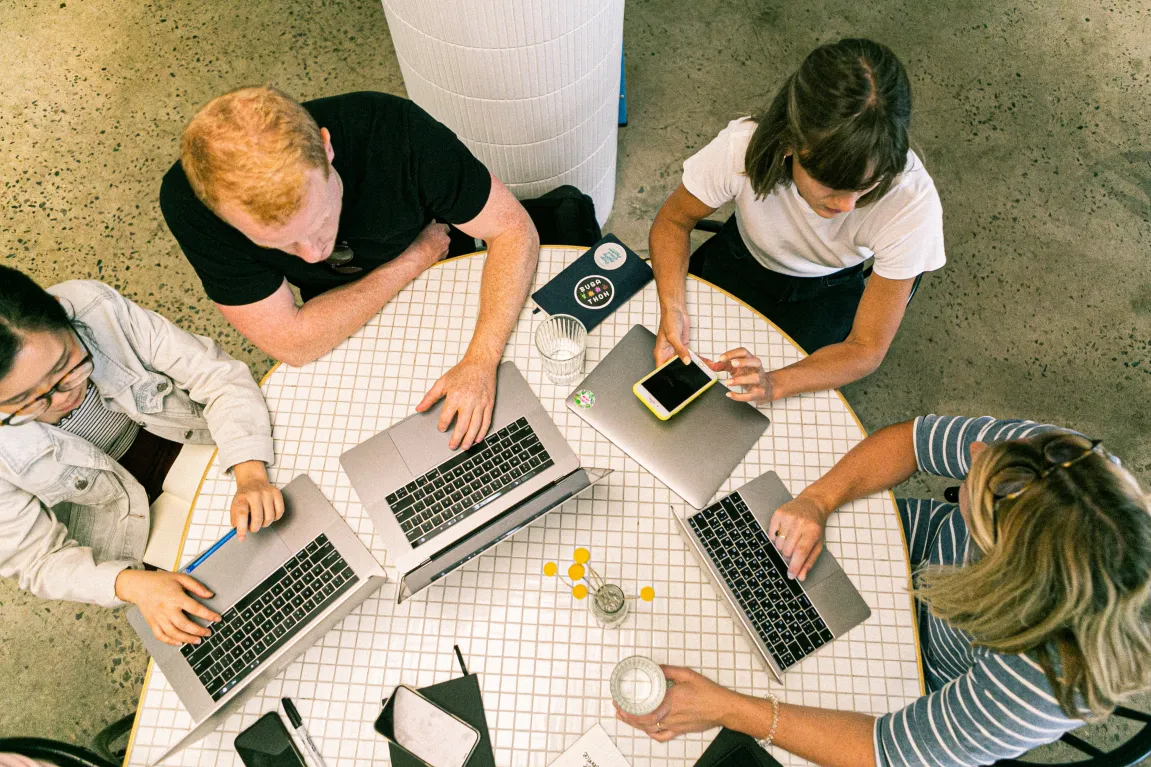 A group of employees gather around a table with laptops