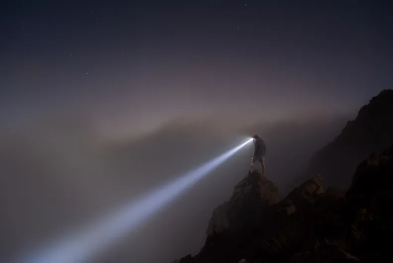 Person standing on a cliff with a flashlight