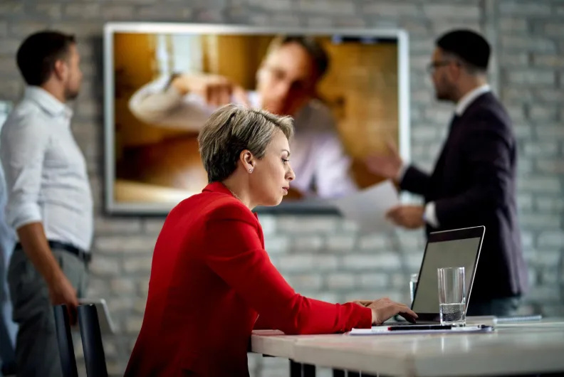 Woman working on laptop with video call in the background