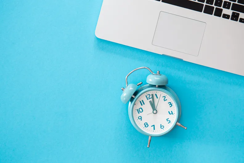 Alarm clock by laptop on blue table