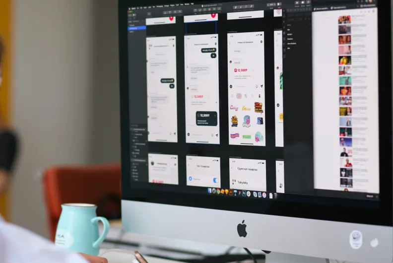 Person working at a desktop computer displaying mobile app interface designs.
