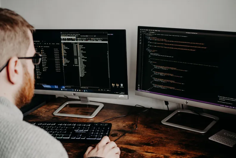 Person working at a desk with two computer monitors displaying code and development files.