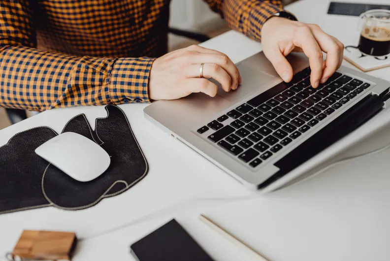 Person working on a laptop at a desk with a mouse and cup of coffee.