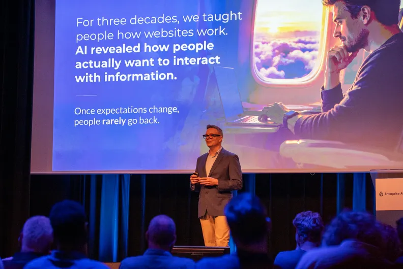 Gleen presenting on stage to a seated audience, with a slide explaining how AI is changing the way people interact with information.